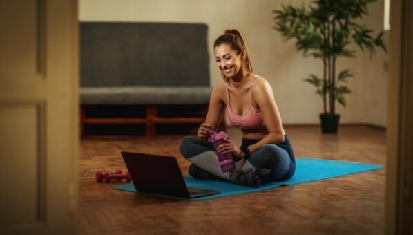 [freepicdownloader.com]-young-smiling-woman-is-watching-internet-tutorial-doing-sports-training-living-room-floor-mat-front-laptop-normal