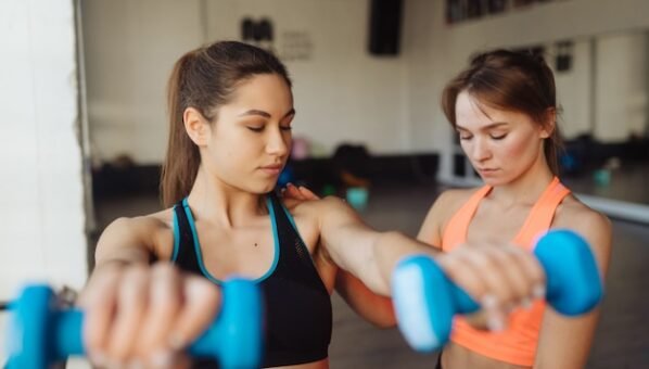 [freepicdownloader.com]-young-woman-personal-trainer-helping-with-workout-gym-woman-doing-exercises-normal